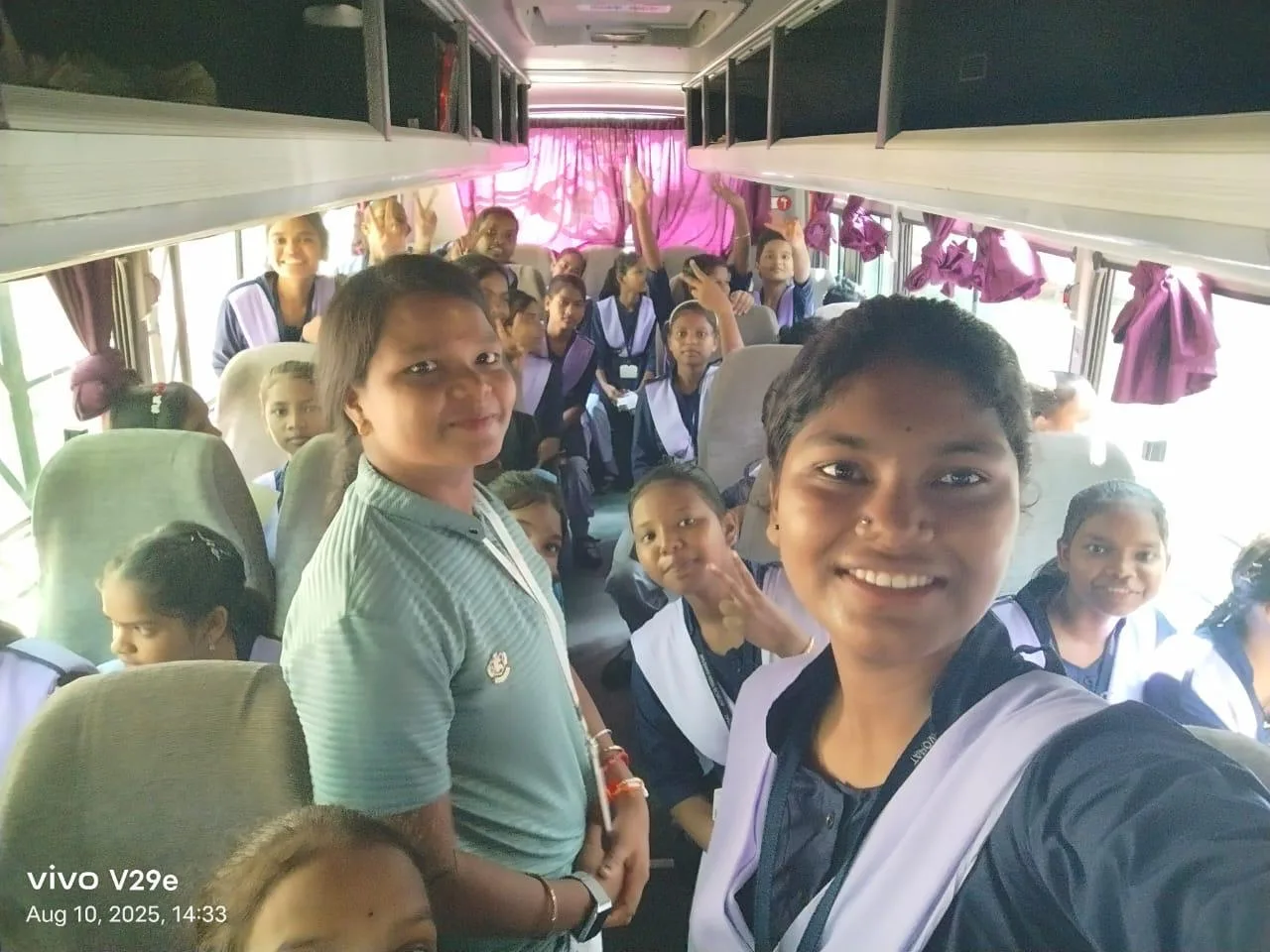 Students smiling together while travelling by bus for an activity.